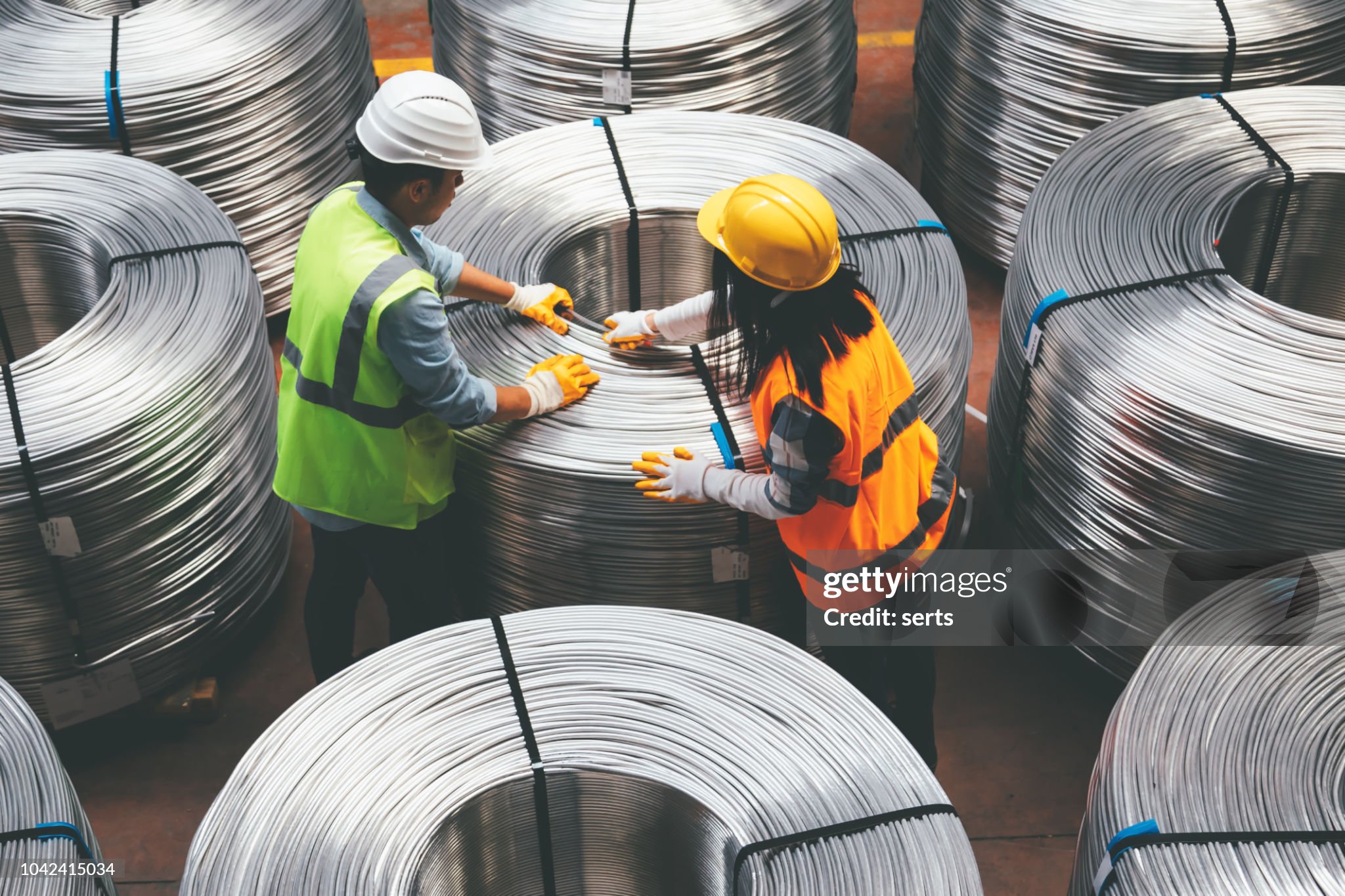 Aerial view of young engineer man and industrial worker woman checking production line and testing quality of steel pipe coils at warehouse section in cable factory. XXXL